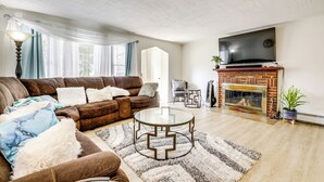 Een woonkamer met een bruine leren bank, een glazen salontafel, een open haard en een aan de muur bevestigde televisie.