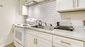 Een keuken met witte kasten, een roestvrijstalen spoelbak en een inbouwoven.