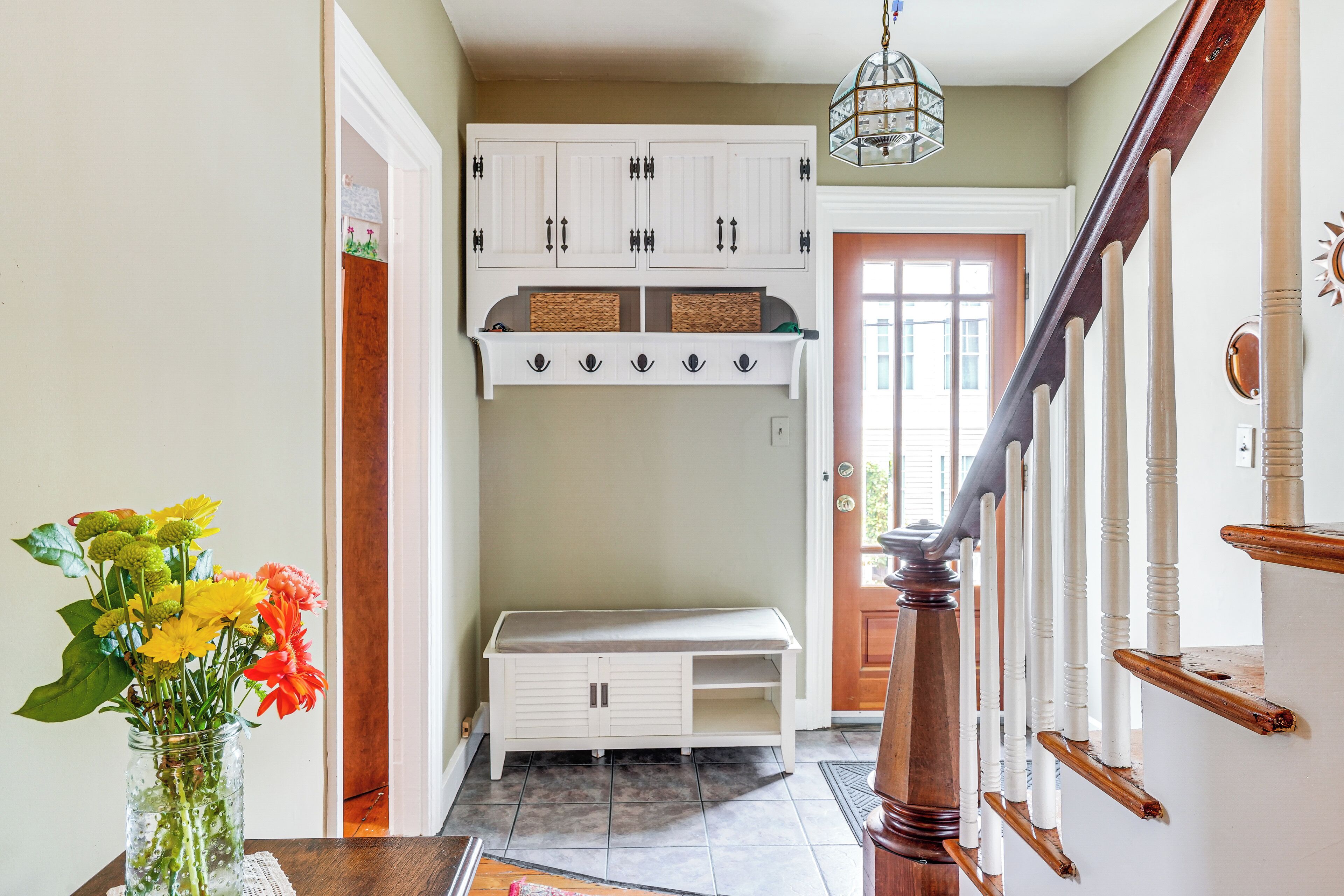 A hallway with a bench, a white cabinet, and a wooden staircase.