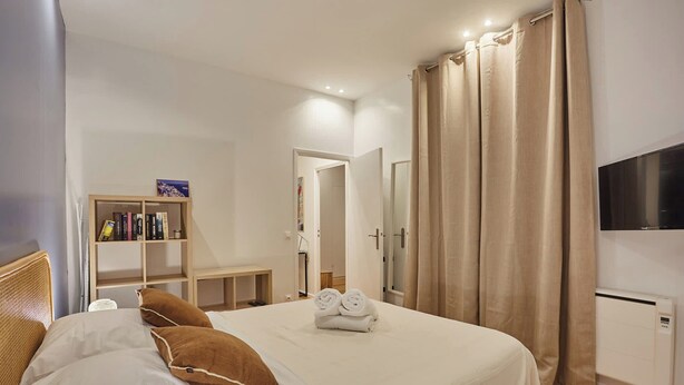 A neatly arranged bedroom with a bed, a bookshelf, a TV, and a wardrobe. - New Apartment Center of Paris (Paris)