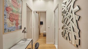 A hallway with a desk, chairs, a lamp, a colorful abstract painting, and a geometric wall art piece. - New Apartment Center of Paris (Paris)