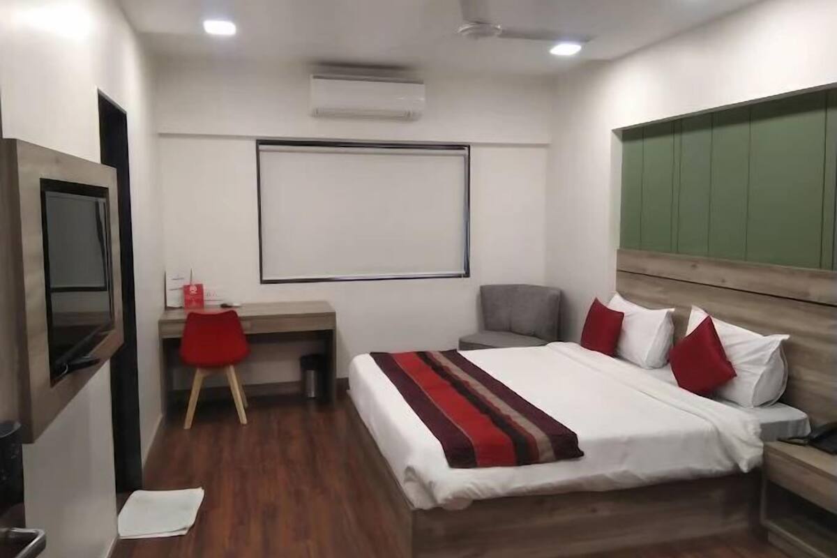 Una camera d'albergo moderna con un letto, una scrivania, una sedia, una TV e un muro verde.