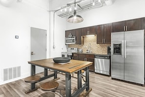 Una cocina moderna con armarios de madera oscura, electrodomésticos de acero inoxidable, una mesa de comedor de madera y una lámpara colgante.