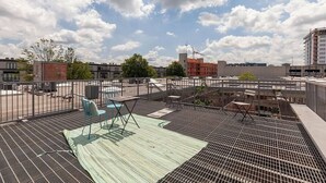 Eine Dachterrasse mit Gitterrostboden, Sitzgelegenheiten im Freien und Blick auf die umliegenden Gebäude.
