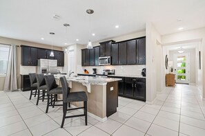 Una cocina moderna con armarios oscuros, una isla central y un comedor con sillas.