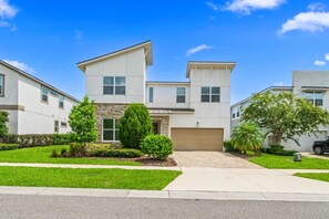 A modern two-story residential building with a garage, a well-maintained lawn, and a clear blue sky.