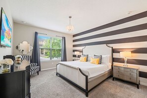 Un dormitorio con cama, mesitas de noche, cómoda, ventana con cortinas y candelabro.