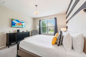A bedroom with a large bed, a television on the wall, a window with curtains, and a radiator.