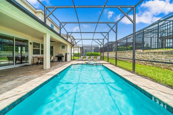 A swimming pool with a covered patio area, a stone wall, and a view of a residential building.