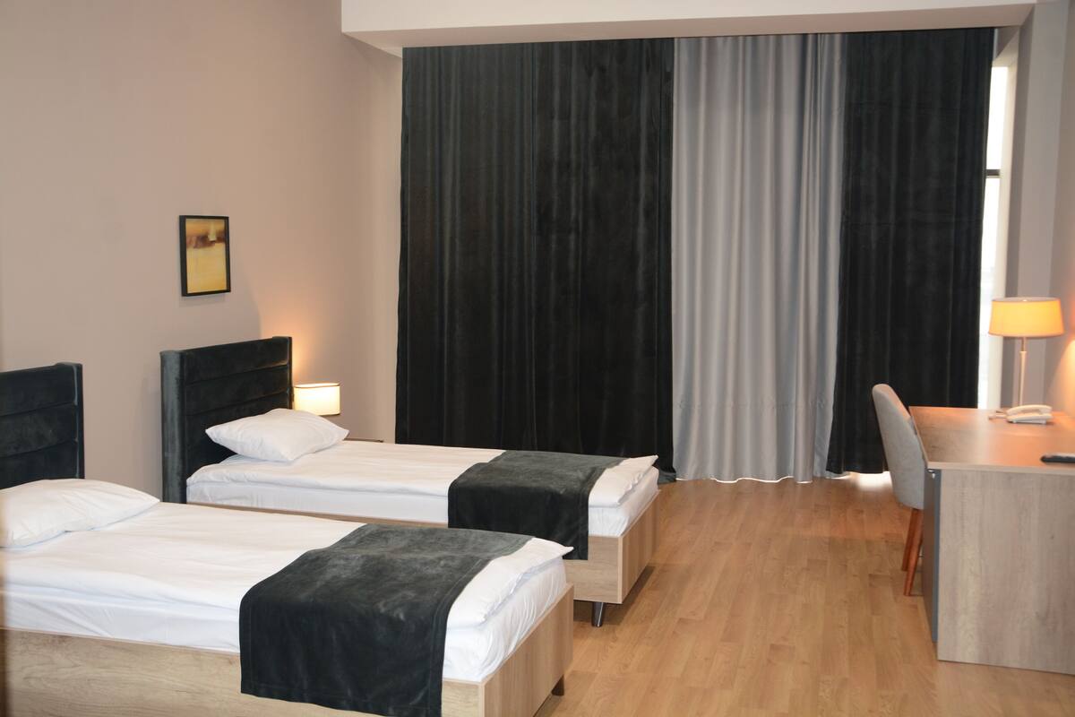 Quarto de hotel com duas camas, uma escrivaninha e uma cadeira.