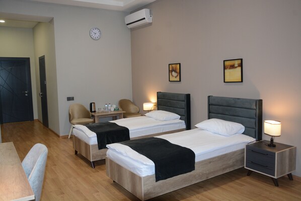 A hotel room with two beds, a desk, a chair, a nightstand with a lamp, a clock, and an air conditioner.
