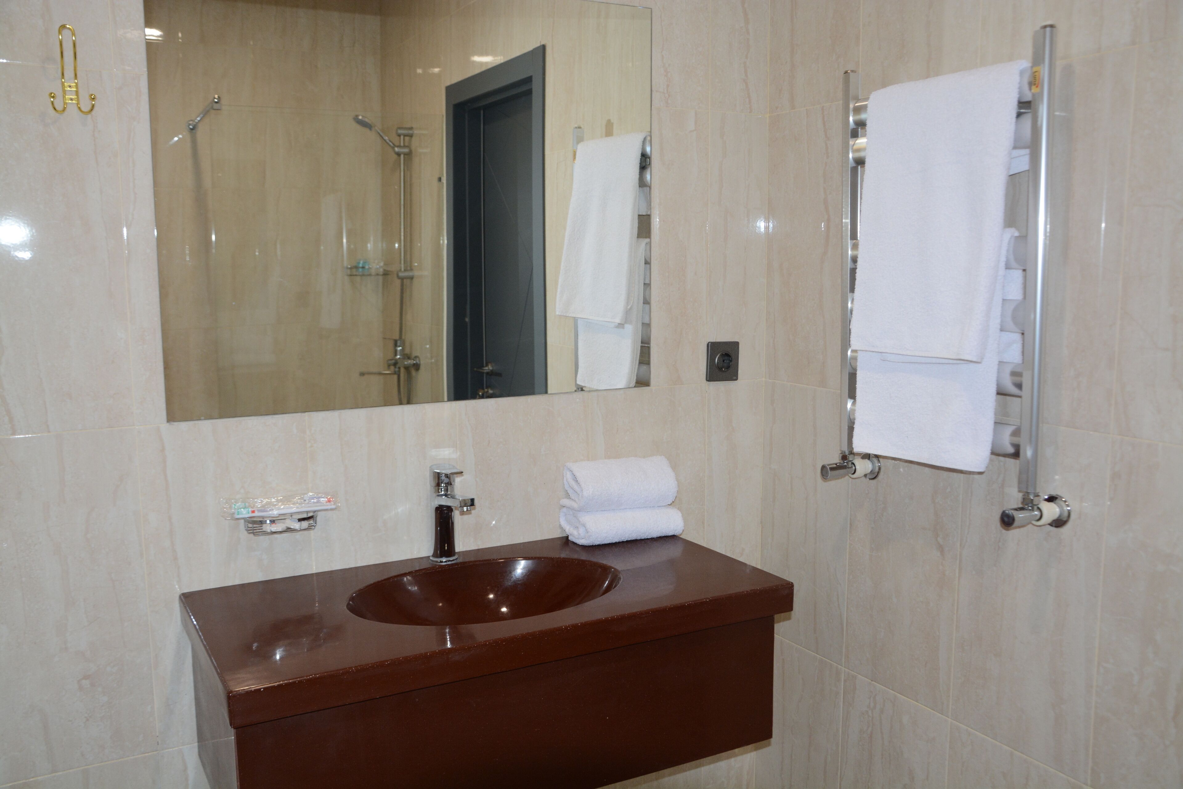 A bathroom with a large mirror, a brown sink, and a towel rack with folded towels.