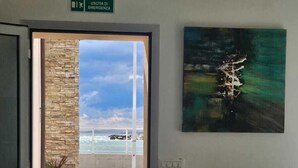 A room with a view of the sea, a painting on the wall, and a sign indicating an emergency exit.