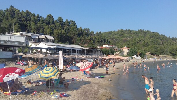 Ein Strand mit Sonnenschirmen, Liegestühlen und Menschen, die im Wasser entspannen.