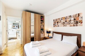 Ein Hotelzimmer mit einem großen Bett, einem Holzschrank, einer Wandcollage und einem durchgegangenen Tür sichtbaren Badezimmer.