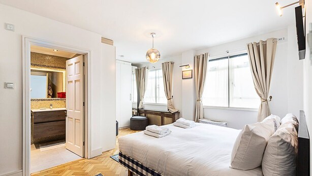 A bedroom with a large bed, a bedside table, a mirror, and a wardrobe. - Chic Marylebone Central Flat (London)