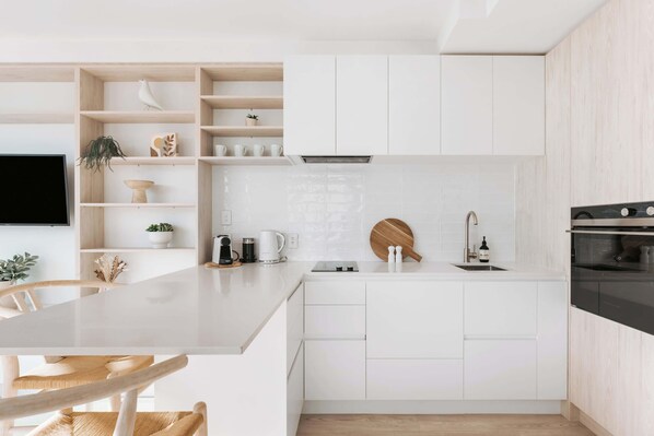 Une cuisine moderne avec des meubles blancs, une table à manger en bois et un téléviseur encastré.