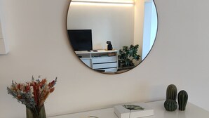 A white console table with a round mirror, a vase with dried flowers, a camera, and decorative objects.
