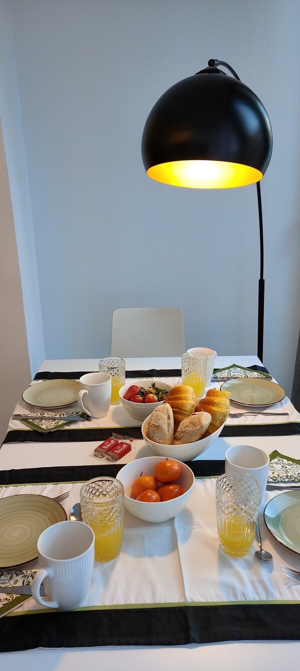 A breakfast table with a bowl of pastries, a glass of orange juice, and a fruit bowl.