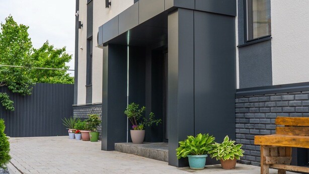 Un edificio moderno con un área exterior cubierta, plantas en macetas y un banco de madera.