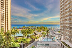 Un grand hôtel avec une piscine, des palmiers et une vue sur la plage et l’océan.