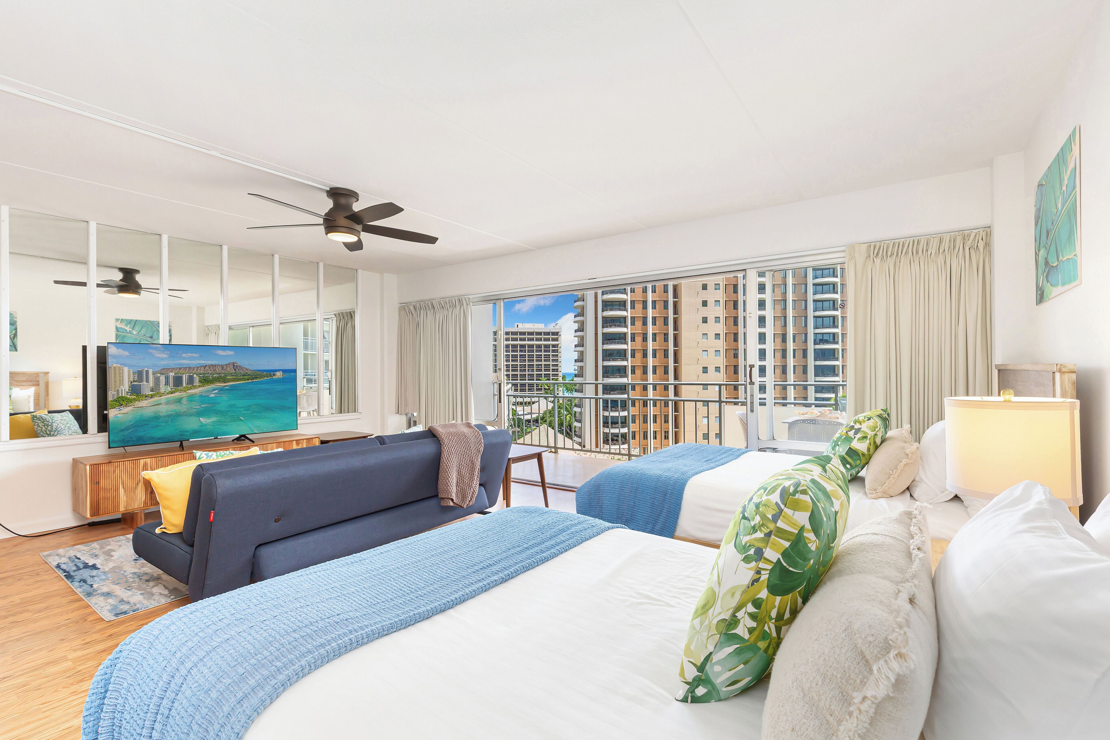 A hotel room with a large bed, a sofa, a TV, and a balcony with a city view.