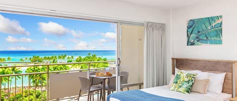 A hotel room with a balcony overlooking a beach, a bed with a wooden headboard, and a table with chairs.