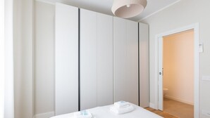 A bedroom with a bed, two towels, a wardrobe, and a door leading to a bathroom.
