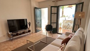 A living room with a TV, sofa, coffee table, and a view of the outside.