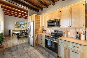 Una cocina con armarios de madera, electrodomésticos de acero inoxidable y un comedor con mesa y sillas.