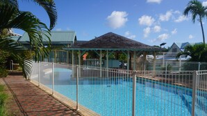 A swimming pool with a fenced area, a covered pavilion, and a brick pathway. - Apartment Dahlia (500 m from the Pointe Marin BEACH, with SWIMMING POOL) (Sainte-Anne)