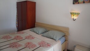 A bedroom with a bed, pillows, a wardrobe, and a wall-mounted light fixture. - Apartment Dahlia (500 m from the Pointe Marin BEACH, with SWIMMING POOL) (Sainte-Anne)