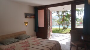 A hotel room with a bed, a desk, and a view of a pool and palm trees. - Apartment Dahlia (500 m from the Pointe Marin BEACH, with SWIMMING POOL) (Sainte-Anne)