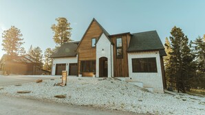 A modern two-story house with a prominent wooden facade, large windows, and a sloped roof.