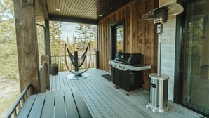 A wooden deck with a grill, a trash can, and a hanging light fixture.