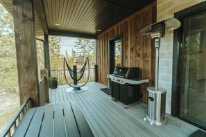 Eine Holzterrasse mit Grill, Mülleimer und einer Hängeleuchte.