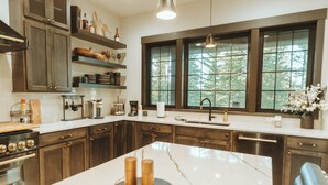 A modern kitchen with dark wood cabinets, a marble island, and a large window with a view of trees.