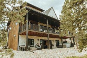 A two-story wooden house with a balcony, outdoor seating, and a stone foundation.