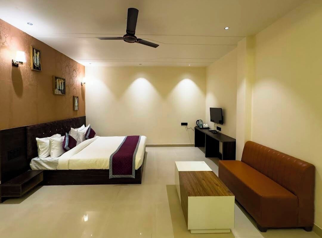 A hotel room with a bed, a sofa, a TV, and a ceiling fan.