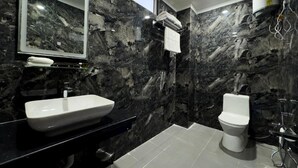 A modern bathroom with a black marble wall, a white sink, a toilet, and a mirror. - HOTEL PARAS CHITTORGARH (Chittorgarh)