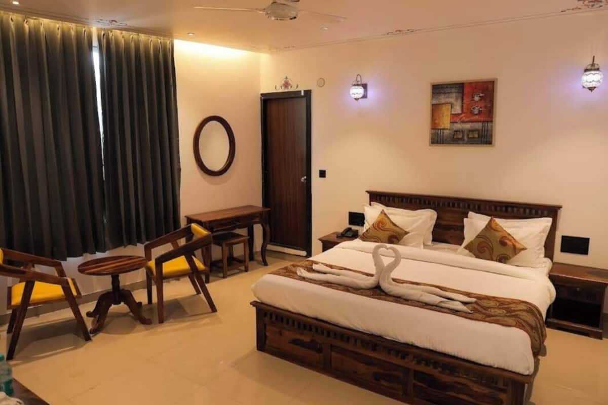 Habitación de hotel con una cama grande, un escritorio, dos sillas, un espejo redondo y una puerta.