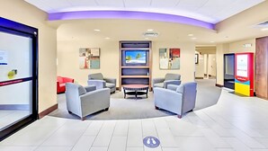 Een hotel lobby met zithoeken, een receptiebalie en een televisiescherm.