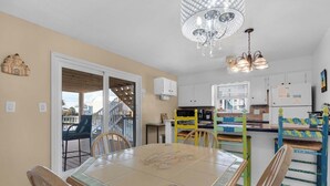 A dining area with a glass-top table, chairs, and a chandelier. - 🌊 Boardwalk F1 | Steps to Gulf, Bayfront Views, Walk to Peg Leg Pete’s 🌊 (Pensacola Beach)