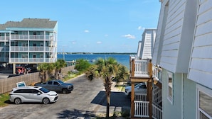 A coastal building with multiple balconies, a parking area with cars, and a view of the sea. - 🌊 Boardwalk F1 | Steps to Gulf, Bayfront Views, Walk to Peg Leg Pete’s 🌊 (Pensacola Beach)