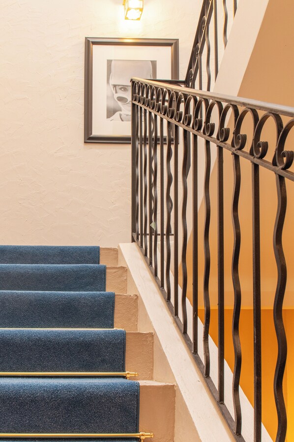 A staircase with blue carpeted steps, a white handrail, and a black metal railing. - Hotel Villa Botanica (Cannes)