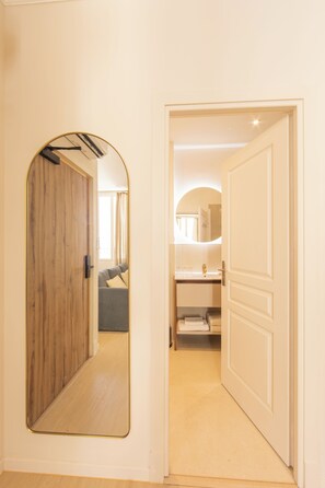 A hallway with a wooden door, a mirror, and a bathroom with a sink and towel rack. - Hotel Villa Botanica (Cannes)