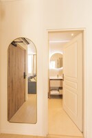 A hallway with a wooden door, a mirror, and a bathroom with a sink and towel rack.