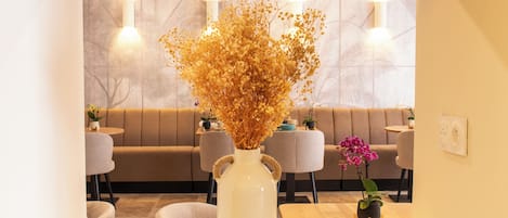 Een witte vaas met gedroogde bloemen op een tafel in een modern interieur, met een bank en stoelen op de achtergrond.