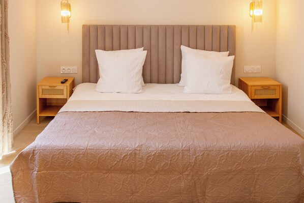 A neatly made bed with a headboard, two bedside tables with lamps, and a remote control on one of the tables. - Hotel Villa Botanica (Cannes)