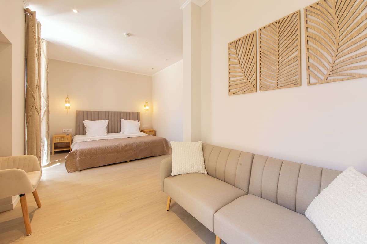 A modern hotel room with a large bed, a sofa, a chair, and a wall-mounted light fixture.